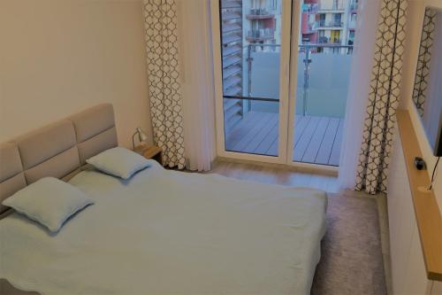 a bedroom with a white bed and a balcony at Blue Sea Apartment in Kołobrzeg