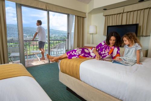 ホノルルにあるCoconut Waikiki Hotelのホテルの部屋のベッドに座っている2人の若い女の子