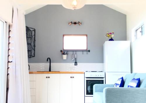 uma cozinha com armários brancos e um frigorífico branco em Piha Tiny House em Piha