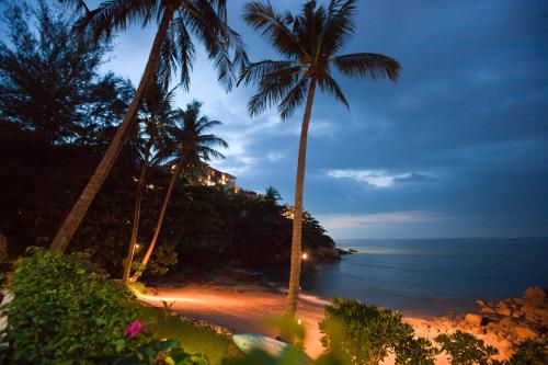 a beach with palm trees and the ocean at night at Kamala Beach Estate Resort - SHA Extra Plus in Kamala Beach