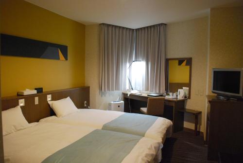 a hotel room with a bed and a desk and a television at Fujisan Station Hotel in Fujiyoshida