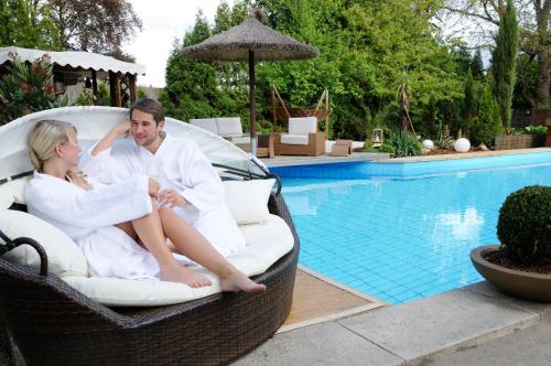 a man and woman sitting in a wicker chair by a swimming pool at Hotel Zur Heimat in Weiden