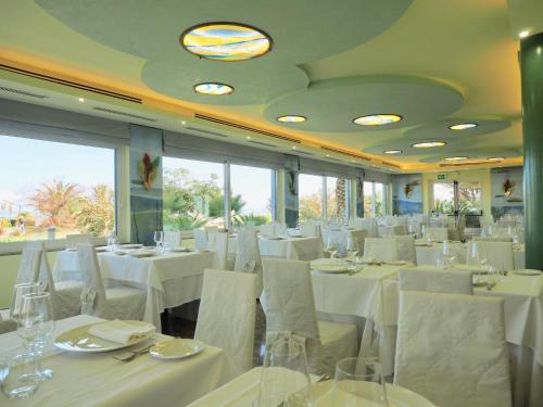 a restaurant with white tables and chairs and windows at Hotel Royal in Fermo