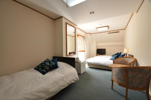 una habitación de hotel con 2 camas y una silla en Hakuba Yamano Hotel en Hakuba
