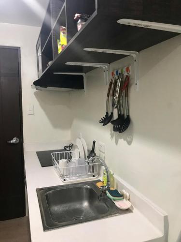 a kitchen counter with a sink and a shelf with utensils at Vinia Residences + Versaflats in Manila