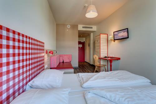 a bedroom with two white beds and a red and white wall at MEININGER Hotel Salzburg City Center in Salzburg