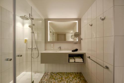 a bathroom with a shower and a sink and a mirror at H+ Hotel Wien in Vienna