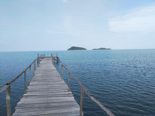 a wooden pier in the middle of a body of water at Tanjong Tinggi Cottage in Sijuk
