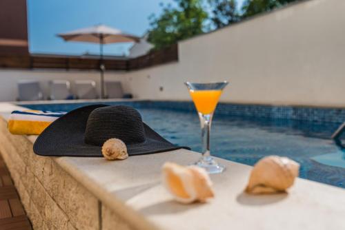 a black hat and a drink on a table next to a swimming pool at Apartment Carpe Diem in Crikvenica