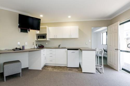 a kitchen with white cabinets and a tv on the wall at Fairley Motor Lodge in Napier
