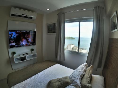 a bedroom with a bed and a window with a television at Porto Real Suites Apto Luxo com vista p/ Mar in Mangaratiba