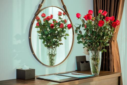 two vases with red roses on a table in front of a mirror at Sun Bay Tuan Chau Hotel in Ha Long