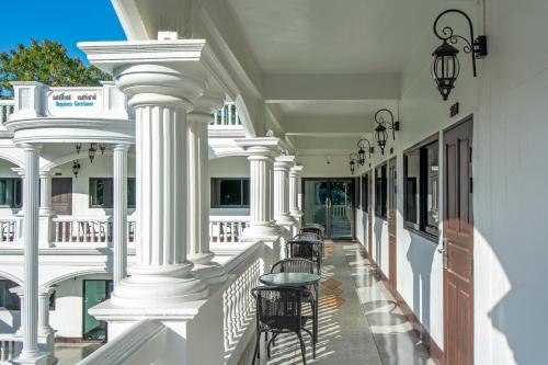 a white building with columns and tables on a balcony at Happiness Guesthouse in Pak Chong
