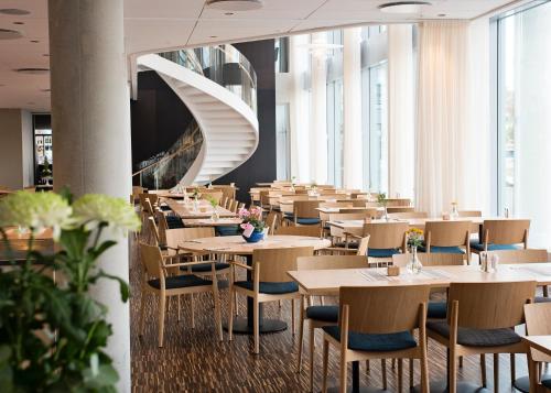 a restaurant with tables and chairs and a spiral staircase at Hotel Öresund Conference & Spa in Landskrona