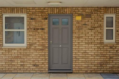 a brick wall with a gray door and two windows at PREMIER SUITES Reading in Reading