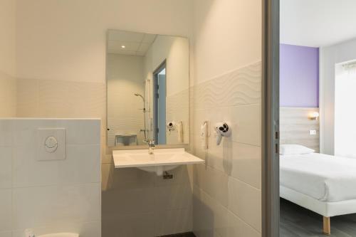 a bathroom with a sink and a mirror and a bed at The Originals City, Hôtel Nevers Centre Gare (Inter-Hotel) in Nevers