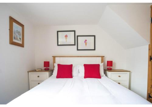 a bedroom with a white bed with two red pillows at Abbey Place Net Loft in Mousehole