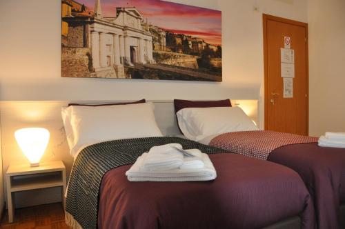 two beds in a room with a painting on the wall at CityWalls Guest House Bergamo in Bergamo