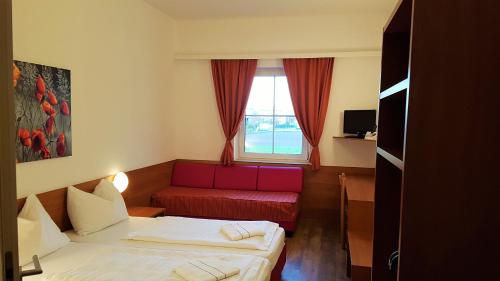 Habitación de hotel con 2 camas y sofá rojo en OEKOTEL Traiskirchen, en Traiskirchen