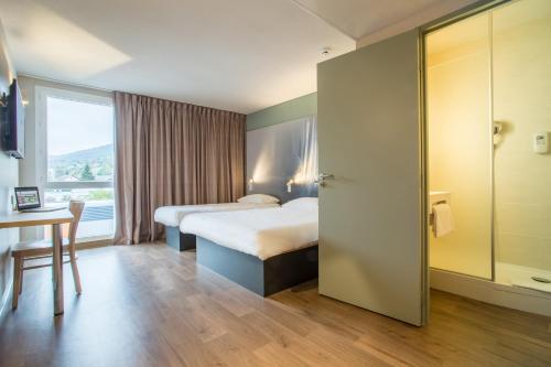 a hotel room with two beds and a table and a window at B&B HOTEL ANNEMASSE Saint-Cergues in Saint-Cergues