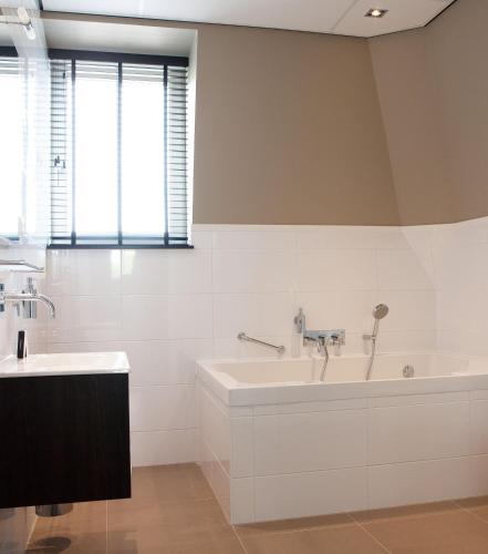 a white bathroom with a tub and a sink at Fletcher Hotel-Restaurant Duinzicht in Ouddorp
