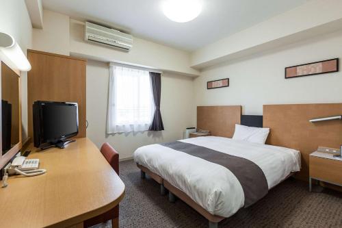 a hotel room with a bed and a desk with a television at Comfort Hotel Central International Airport in Tokoname