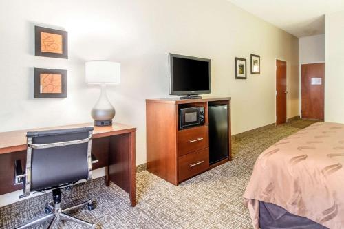 a hotel room with a desk and a bed and a television at Quality Suites in Corbin