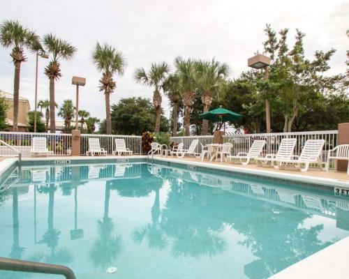a swimming pool with chairs and a umbrella and palm trees at Sleep Inn -Daytona Beach I-95 Exit 268 in Ormond Beach