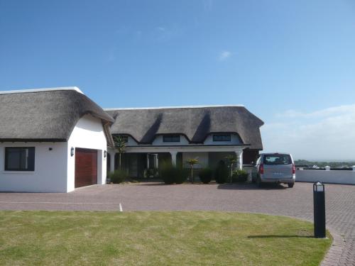a house with a thatched roof with a car parked in front at St Francis Golf Lodge in St Francis Bay