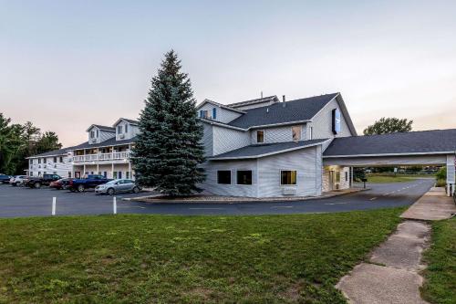 a white house with a tree in a parking lot at Rodeway Inn in Ludington