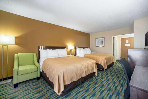 a hotel room with two beds and a green chair at Quality Inn Near Six Flags St. Louis in Pacific