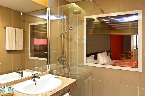 uma casa de banho com um lavatório e um chuveiro com um espelho. em Pestana Tropico Ocean & City Hotel em Praia