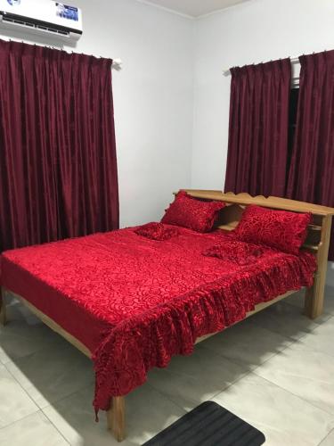 Schlafzimmer mit einem roten Bett und burgunderroten Vorhängen in der Unterkunft Zeedijk Resort Nickerie in Nieuw Nickerie