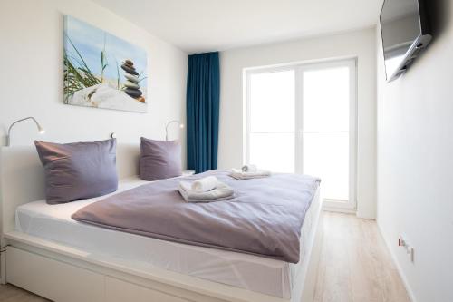 a white bedroom with a large bed with a window at Hafenlodge in Olpenitz