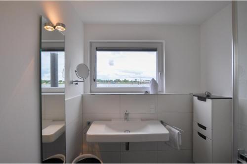 ein weißes Bad mit einem Waschbecken und einem Fenster in der Unterkunft Schwimmendes Haus Haithabu in Olpenitz