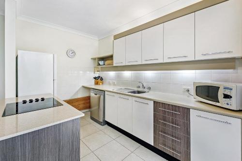 a kitchen with white cabinets and a microwave at Smugglers On The Beach in Coffs Harbour