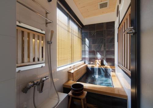 a bathroom with a tub and a sink and a window at CHAHARU Hanare Dogo Yumekura in Matsuyama