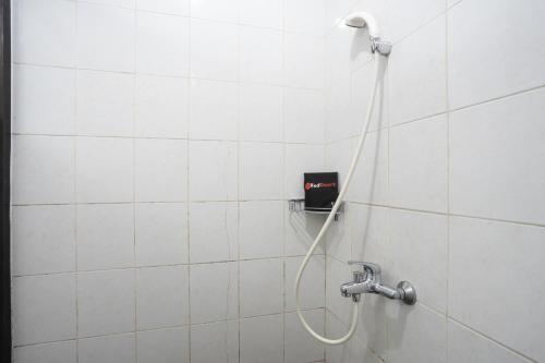 a shower in a white tiled bathroom with a hose at RedDoorz near Eka Hospital BSD City in Tangerang