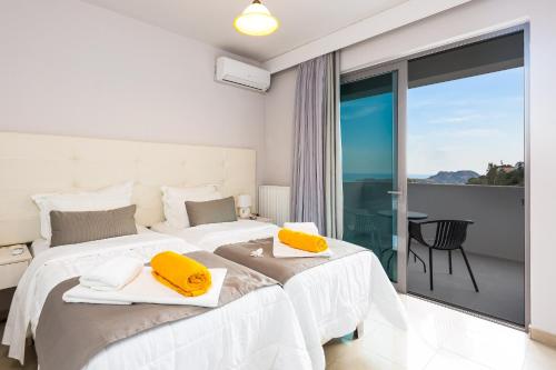 a white bedroom with two beds and a balcony at Sunset Maisonettes in Plakias
