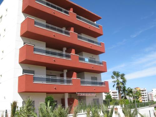 um edifício vermelho com palmeiras em frente em Arenales Playa by Mar Holidays em Arenales del Sol