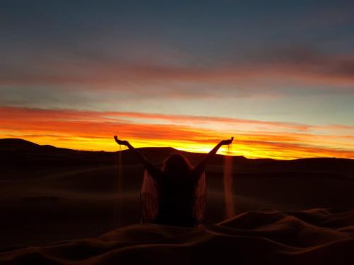 a woman standing in the desert with her arms up at sunset at Berber Camp in Merzouga