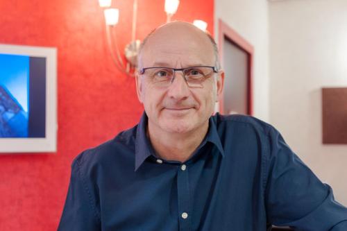 a man with glasses sitting in a room at The Originals City, Hôtel Éden, Rouen Nord in Bois-Guillaume