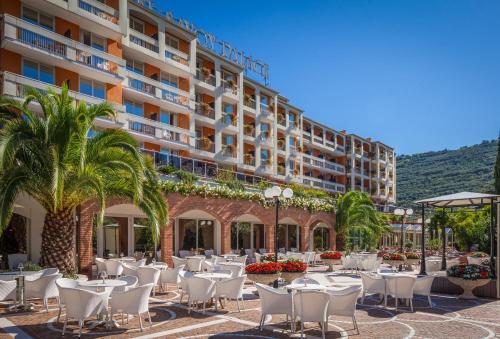 a hotel patio with tables and chairs and palm trees at Hotel Savoy Palace - TonelliHotels in Riva del Garda