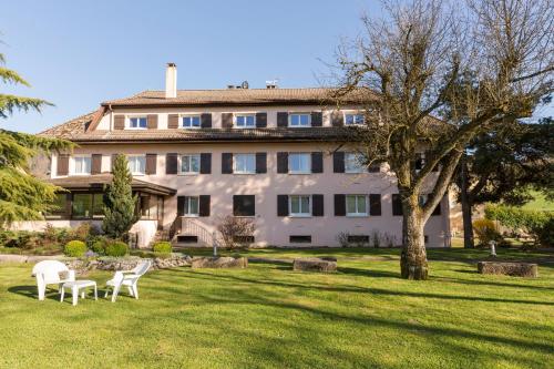 a large building with two white chairs in the grass at The Originals City, Hôtel Rey du Mont Sion, Saint-Julien-en-Genevois Sud in Saint-Blaise