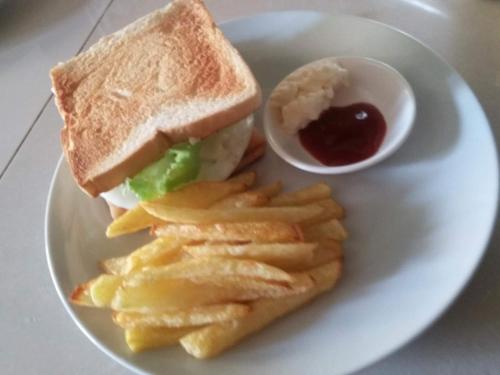 a plate with a sandwich and chips and a cup of ketchup at Guanna's Place Room and Resto Bar in Malapascua Island