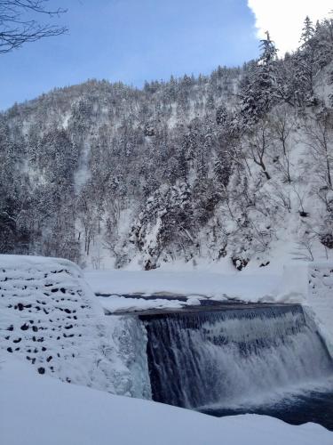 a waterfall covered in snow with a mountain in the background at Shikishimaso in Higashikawa
