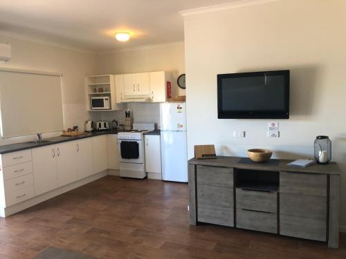 a kitchen with white cabinets and a tv on the wall at The Sundowner Cabin & Tourist Park in Whyalla