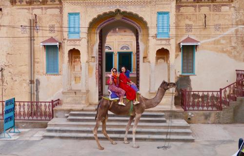 duas pessoas montadas num camelo em frente a um edifício em Mandawa Kothi em Mandawa