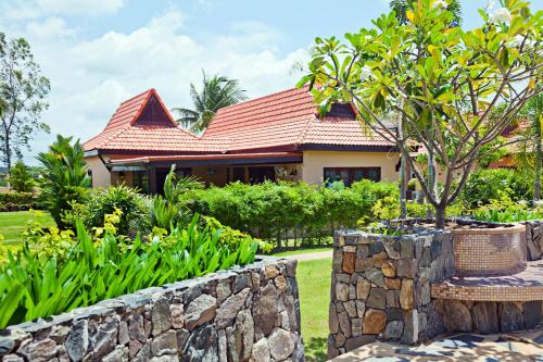 a house with a stone wall and a tree at Family-friendly house, a few steps from the pool and close to the ocean. in Mae Pim