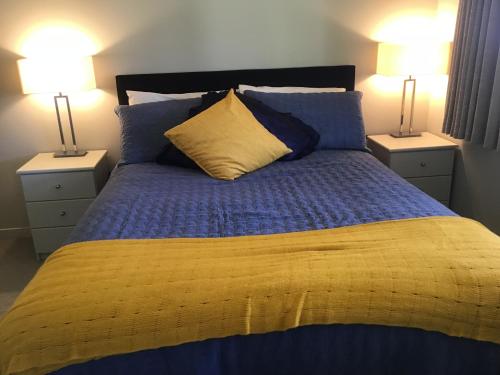 a bed with blue and yellow sheets and two lamps at Treetops On Heta in New Plymouth